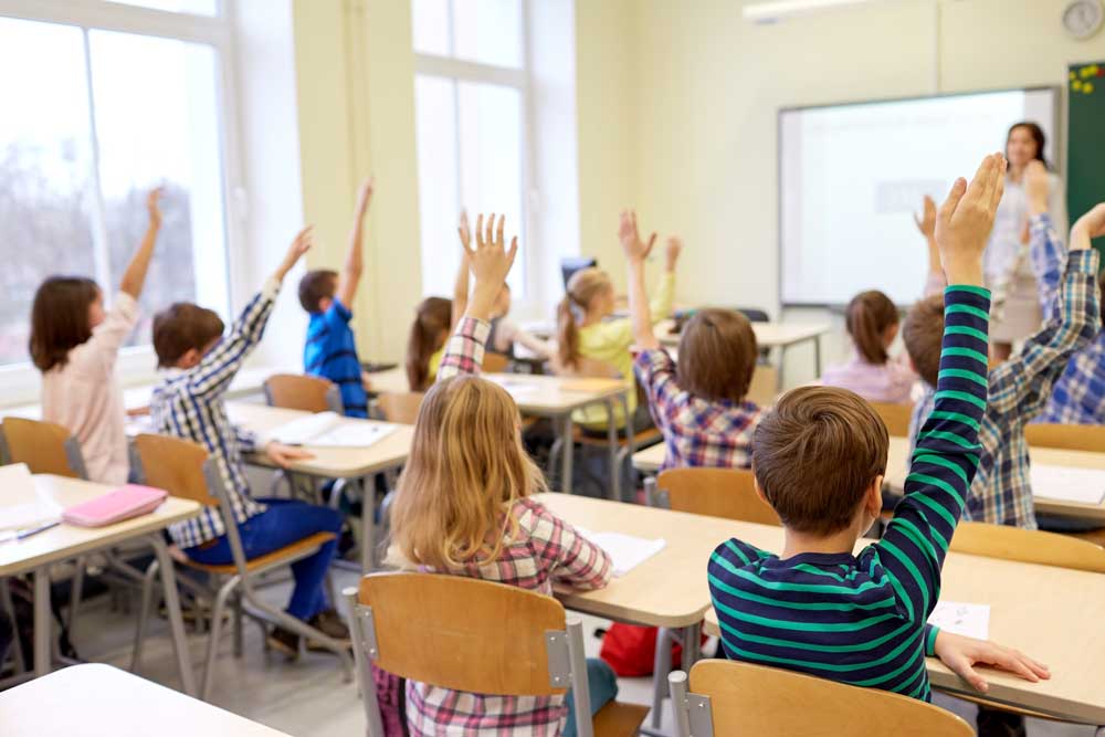 children in a classroom raising their hands