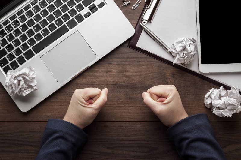 two clenched fists on table in front of a laptop